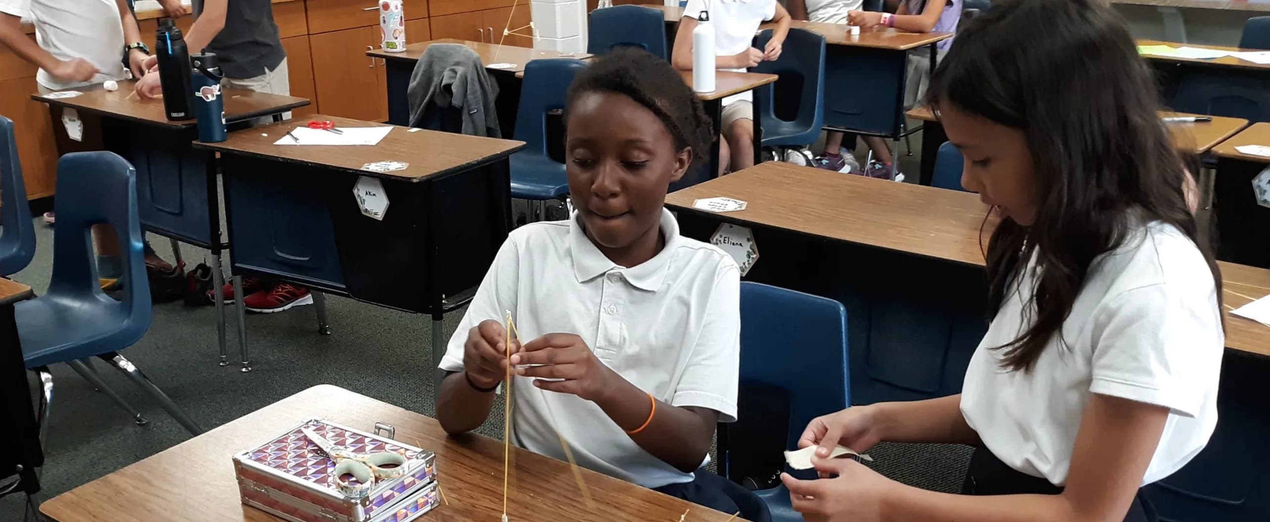 Two students build a spaghetti tower at their classroom desks