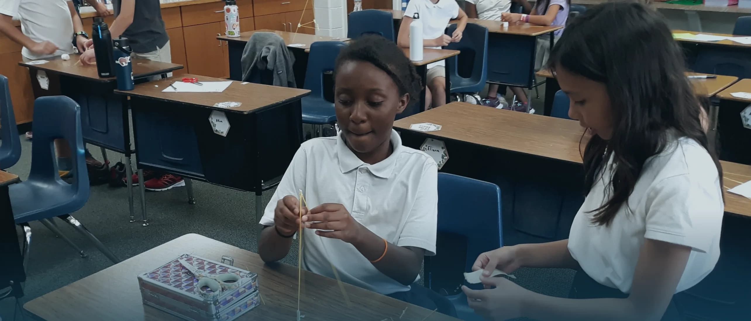 Two students build a structure from spaghetti at their desks