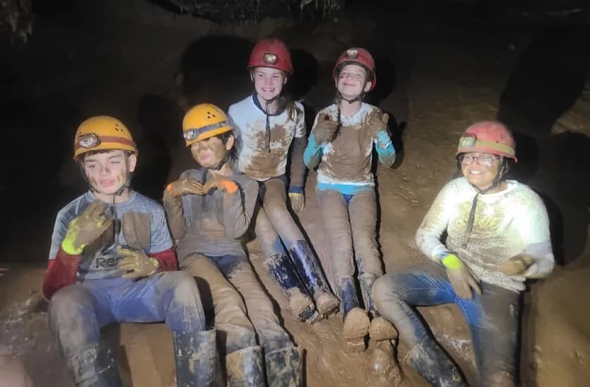Grade 6 students in caving helmets, covered in mud, inside Mammoth Cave