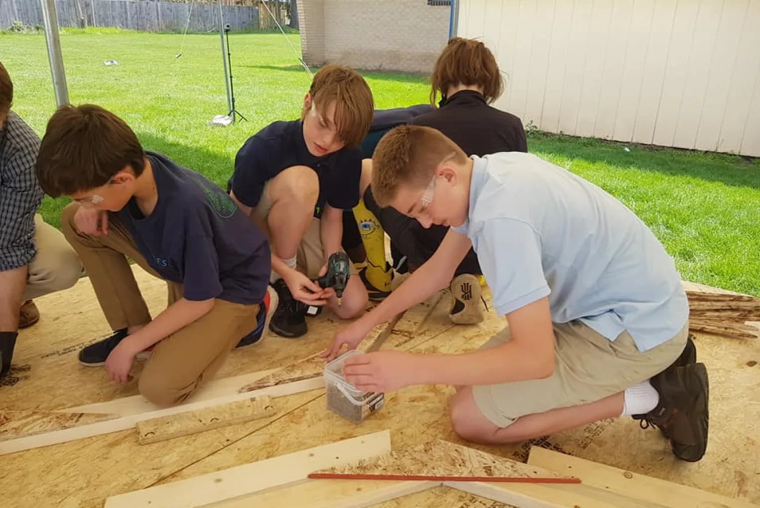 Students in safety glasses use a drill on a woodworking project