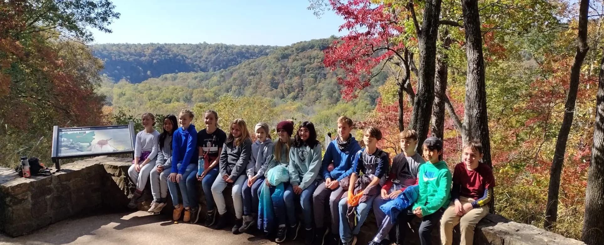 Students sit together at a scenic overlook above an autumn forest