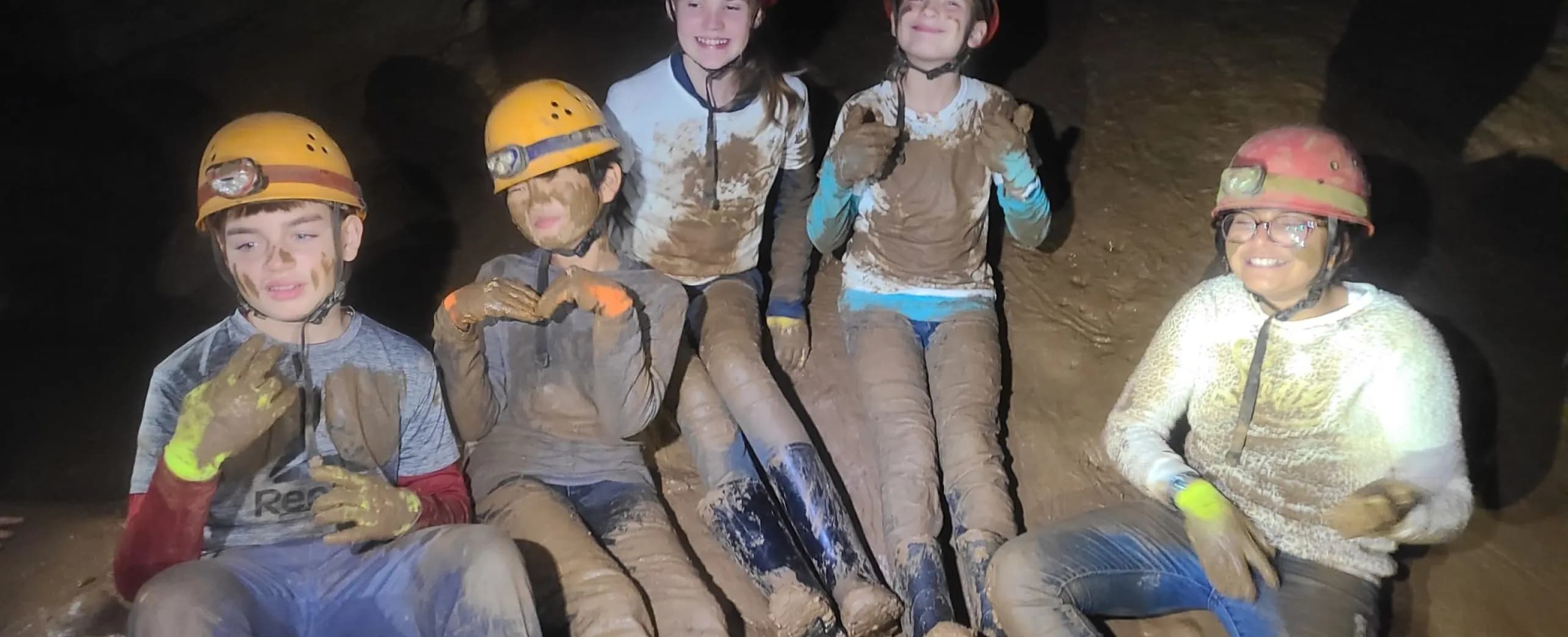 Grade 6 students in caving helmets, covered in mud, inside Mammoth Cave